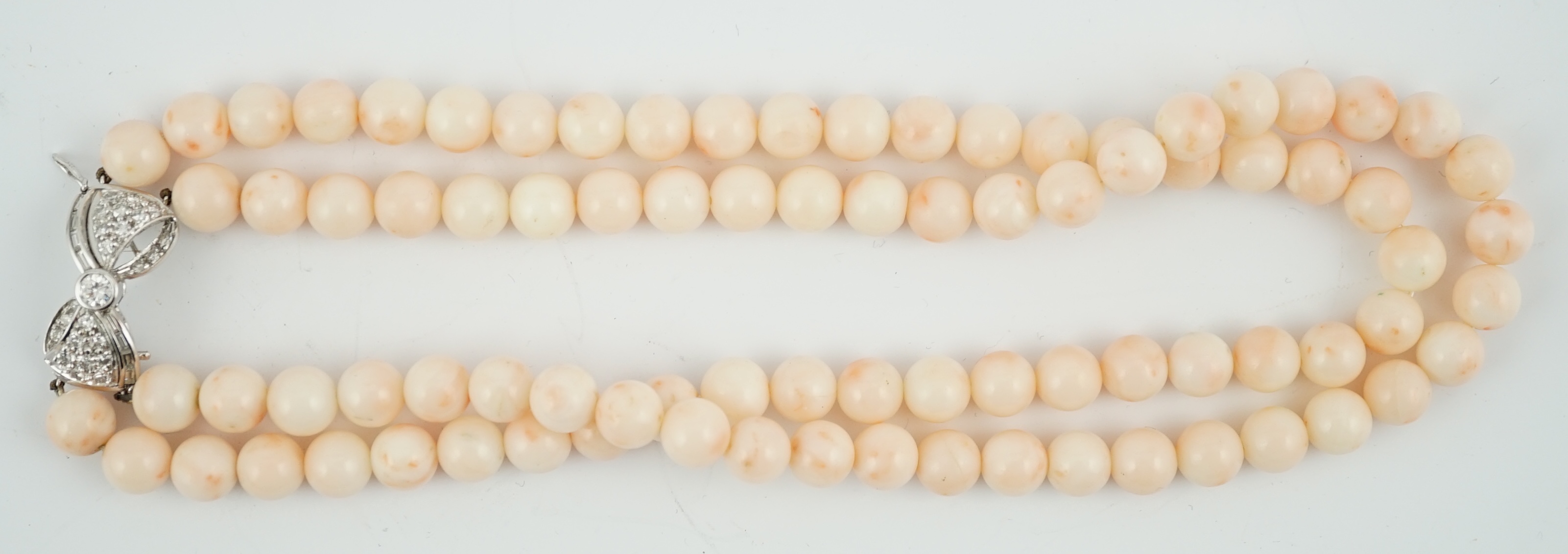 A double strand pale pink coral bead choker necklace, with round and baguette cut diamond cluster set bow shaped 18k white gold clasp